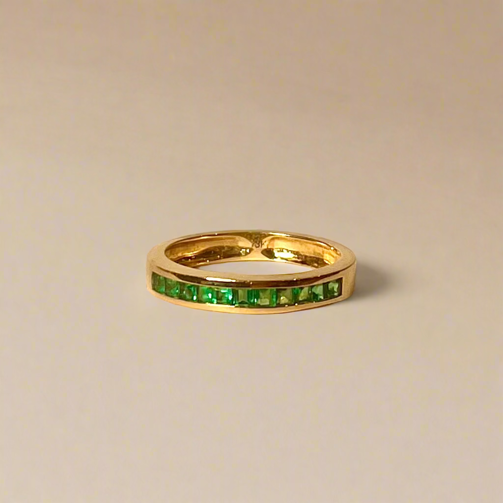 Gold ring with green gemstones on a beige background