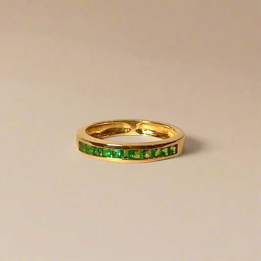 Gold ring with green gemstones on a beige background